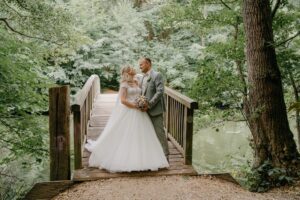 Braut Sarah und Bräutigam Norman stehen auf einer Holzbrücke im Grünen. Sarah trägt ein romantisches A-Linien-Brautkleid mit Spitzenoberteil und voluminösem Tüllrock aus dem Hochzeitsspeicher an der Elbe.