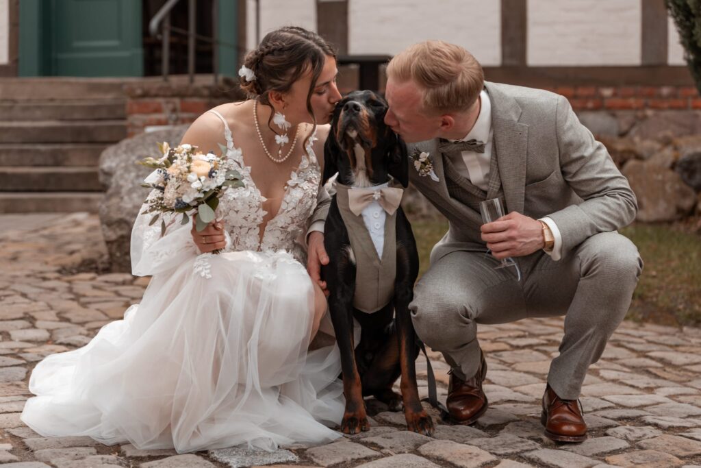 Braut im romantischen Brautkleid mit Spitze und Tüll neben Bräutigam und Hund